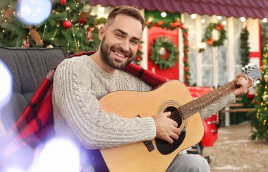 Genç adam Noel arifesinde dışarıda gitar çalıyor.