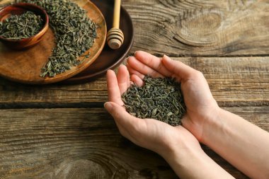 Ahşap arka planda kuru yeşil çay yaprakları olan kadın.