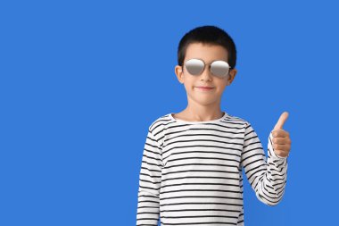 Şık güneş gözlüklü yakışıklı çocuk, arka planda baş parmağını kaldırıyor.