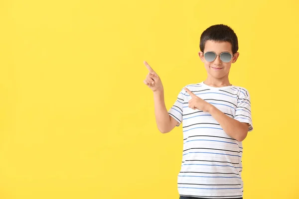 Söt Pojke Med Snygga Solglasögon Pekar Något Mot Färg Bakgrund — Stockfoto