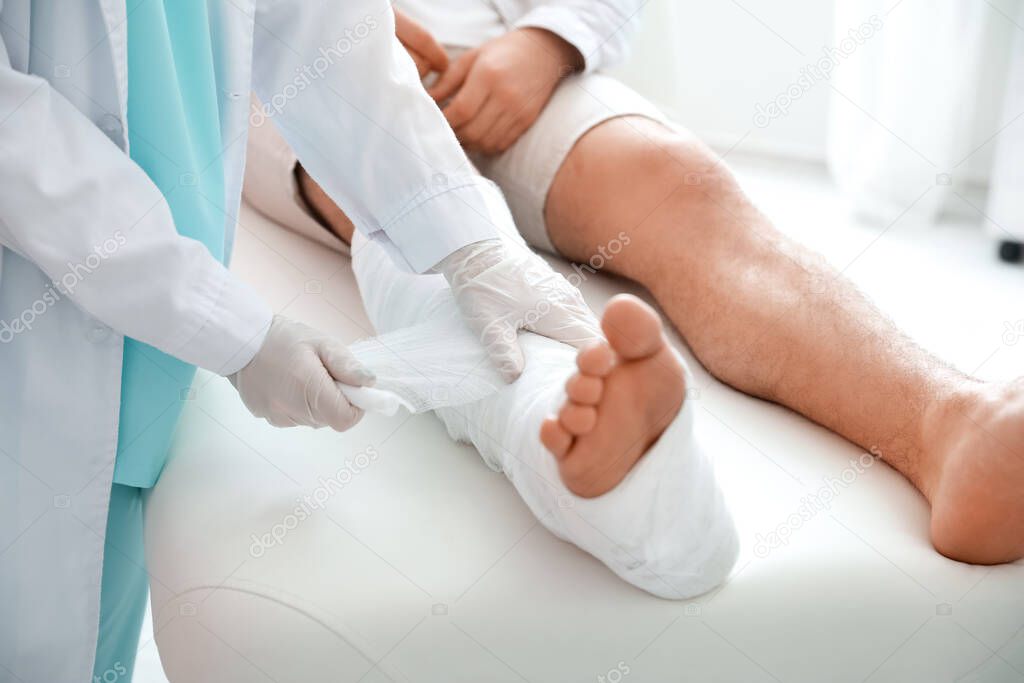 Doctor putting broken leg of young man in plaster