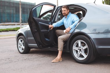 Yakışıklı adam modern arabadan iniyor.