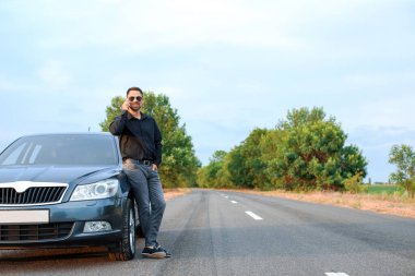 Modern arabasının yanında cep telefonuyla konuşan yakışıklı bir adam.