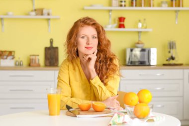 Mutfakta taze portakal suyu ve meyve suyu olan güzel genç bir kadın.