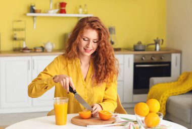Güzel genç bayan mutfakta taze portakal kesiyor.