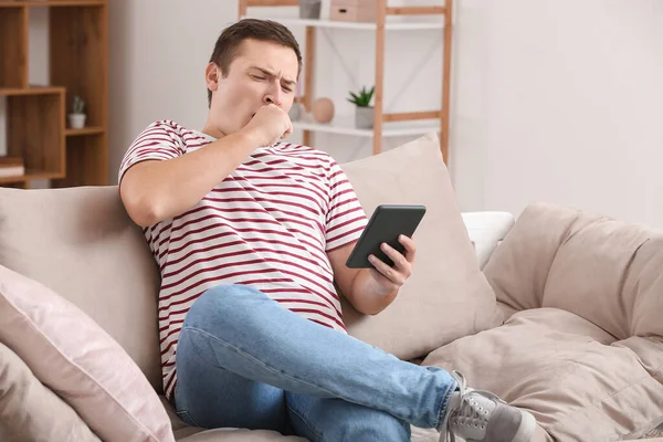 Young man reading boring e-book at home