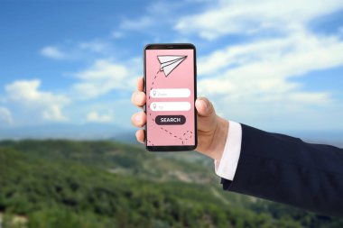Cep telefonlu bir işadamı açık havada uçuş biletleri ayırtıyor.