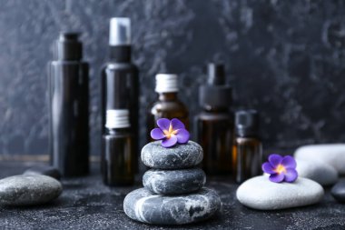 Koyu arkaplanda çiçek ve kozmetik şişeleri olan spa taşları