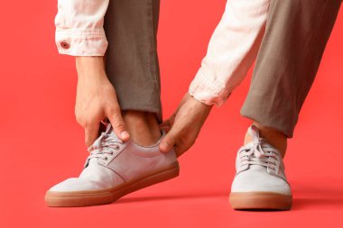 Genç adam renkli arka planda şık ayakkabılar giyiyor.