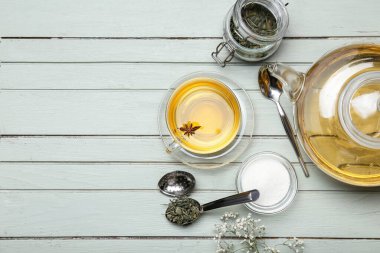 Bir fincan aromatik içecek, çaydanlık ve bir kavanoz kuru çay, ahşap arka planda.