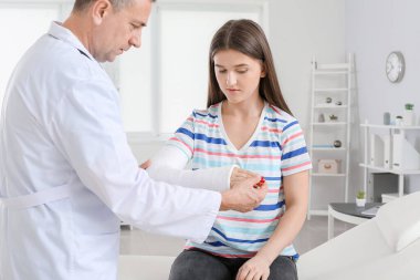 Kol kırığı olan genç bir kadın klinikte doktoru ziyaret ediyor.