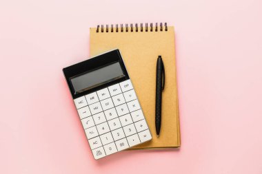 Renk arkaplanı üzerinde dijital hesap makinesi, defter ve kalem