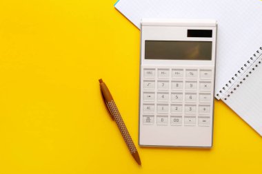 Renk arkaplanı üzerinde dijital hesap makinesi, defter ve kalem