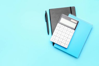 Renk arkaplanı üzerine dijital hesap makinesi, not defterleri ve kalem