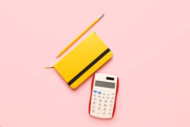 Renk arkaplanı üzerinde dijital hesap makinesi, defter ve kalem