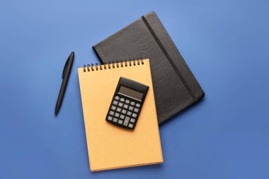 Renk arkaplanı üzerine dijital hesap makinesi, not defterleri ve kalem