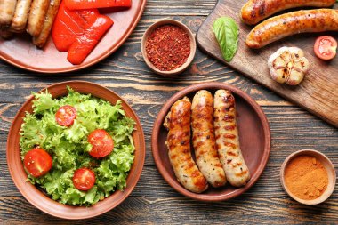 Ahşap masada lezzetli ızgara sosis, sebze ve baharat tabağı.