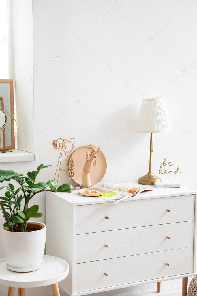 Wooden hand with female jewelry on chest of drawers in interior of room