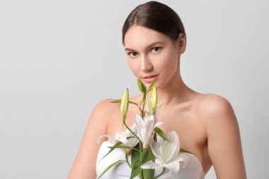 Açık arkaplanda taze zambakları olan güzel genç bir kadın.