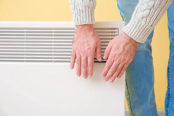 Young man warming hands near electric heater. Concept of heating season