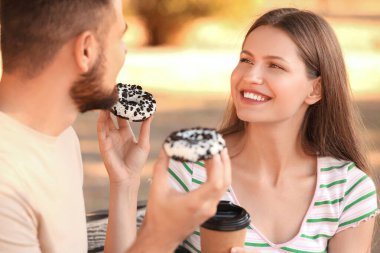 Genç bir çift tatlı çörekler yiyor ve dışarıda kahve içiyor.