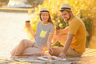 Genç bir çift tatlı çörekler yiyor ve nehir kenarında kahve içiyor.