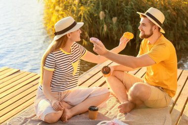 Genç bir çift tatlı çörekler yiyor ve nehir kenarında kahve içiyor.