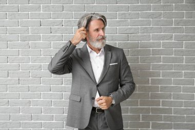 Resmi takım elbiseli olgun bir adam tuğla arka planda saç tarıyor.