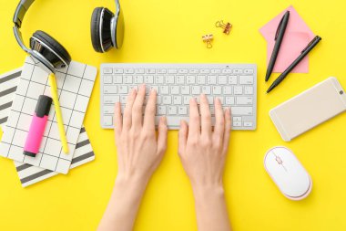 Renk arkaplanı üzerinde bilgisayar klavyesi, aygıtlar ve kırtasiye malzemesi olan kadın elleri