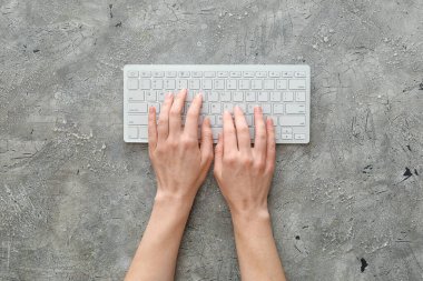Gri arkaplanda bilgisayar klavyesi olan kadın elleri