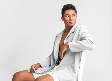 Beyaz arka planda oturan şık genç Afro-Amerikalı adam.