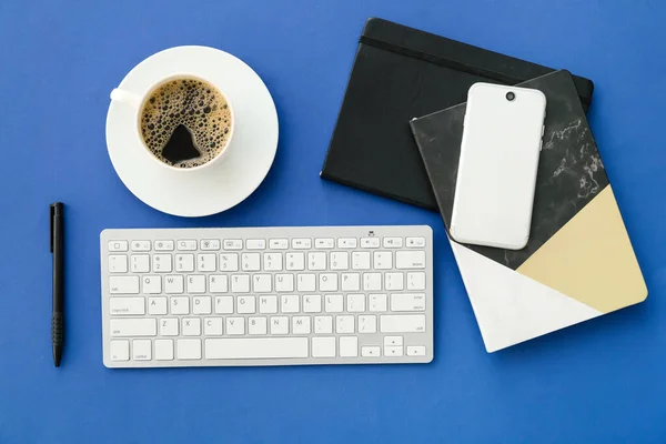 Computer keyboard, cup of coffee and stationery on color background