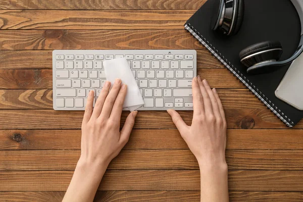 Woman cleaning computer keyboard on wooden background