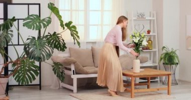 Masaya bir buket güzel zambak koyduktan sonra dergi okuyan genç bir kadın.