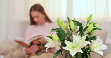 Bir buket güzel zambak, dergi okuyan genç bir kadın odasında.