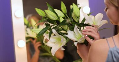 Bir buket güzel zambakla aynaya bakan genç bir kadın.