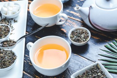 Composition with cups of green tea, teapot and dry leaves on wooden background