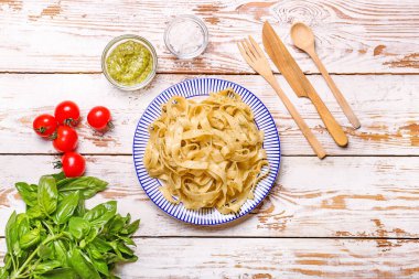 Lezzetli makarna, pesto sosu ve ahşap arka planda malzemelerle dolu bir tabak.