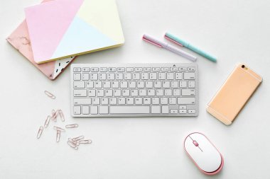 Beyaz arkaplanda fare, kırtasiye ve cep telefonu bulunan bilgisayar klavyesi