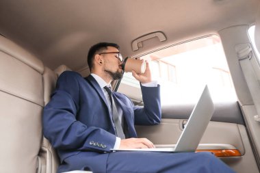 Bilgisayarlı başarılı iş adamı modern arabada kahve içiyor.