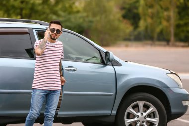 Modern arabanın yanında cep telefonuyla konuşan yakışıklı bir adam.