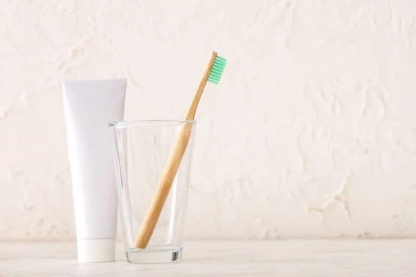 Holder with wooden toothbrush and toothpaste on table in bathroom
