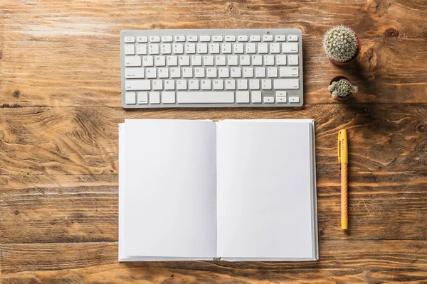 Composition with blank book and computer keyboard on wooden table