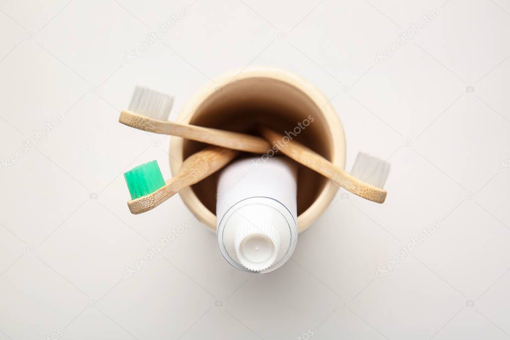 Holder with wooden toothbrushes and toothpaste on light background
