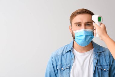 Işık arka planında kızılötesi termometresi olan bir adam ve el. Coronavirüs salgını