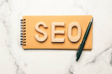 Beyaz arkaplanda defter ve kalemle SEO kısaltması