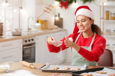Genç bir kadın Noel arifesinde mutfakta lezzetli zencefilli kurabiyeler pişiriyor.