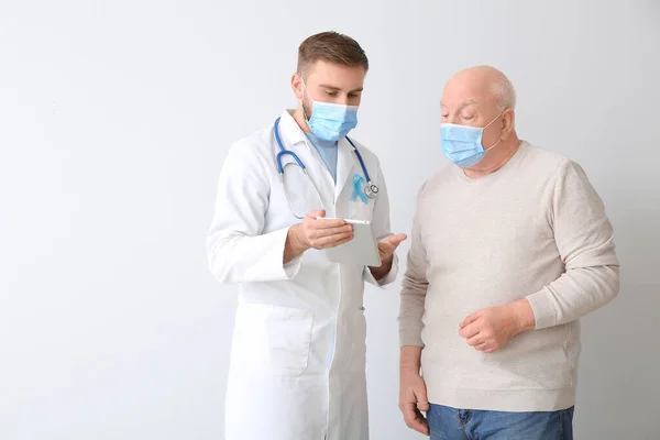 Doctor with tablet computer and senior man on light background. Prostate cancer awareness concept