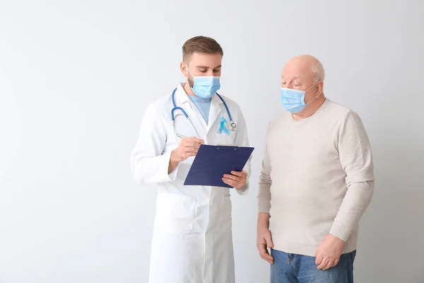 Doctor and senior man on light background. Prostate cancer awareness concept
