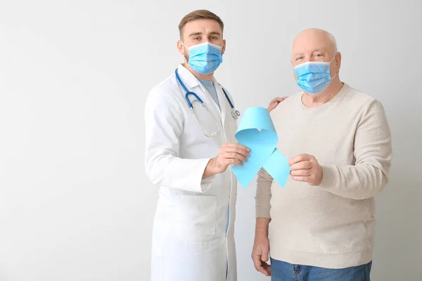 Doctor and senior man with blue ribbon on light background. Prostate cancer awareness concept